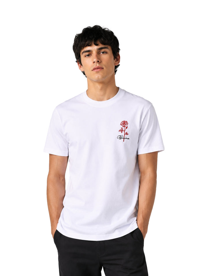 Hombre vistiendo playera blanca de manga corta con un pequeño estampado de rosa roja en el pecho.