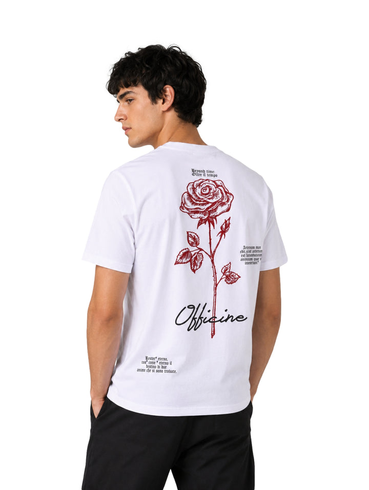 Hombre vistiendo playera blanca de manga corta con un pequeño estampado de rosa roja en el pecho.