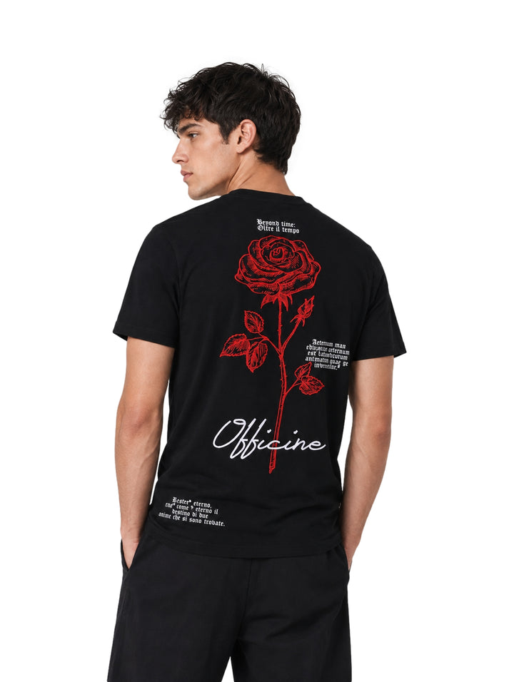 Hombre vistiendo playera negra de manga corta con un pequeño estampado de rosa roja en el pecho.