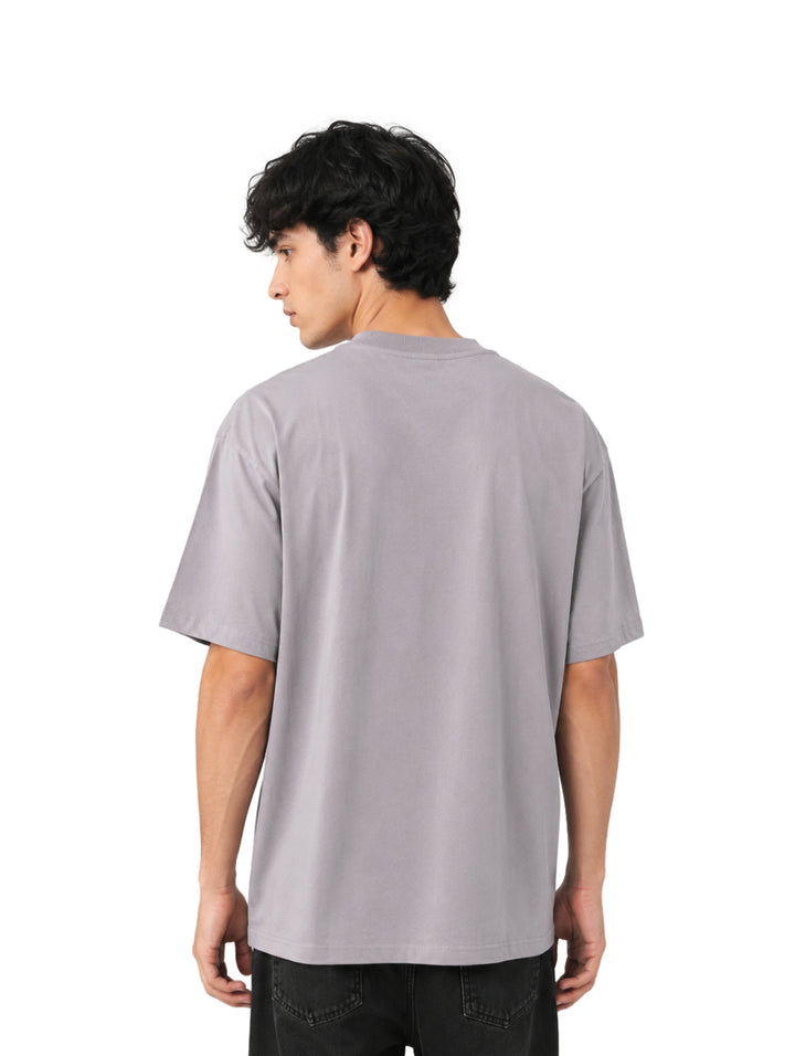 Hombre vistiendo playera color gris de corte amplio con estampado gráfico negro en el pecho.