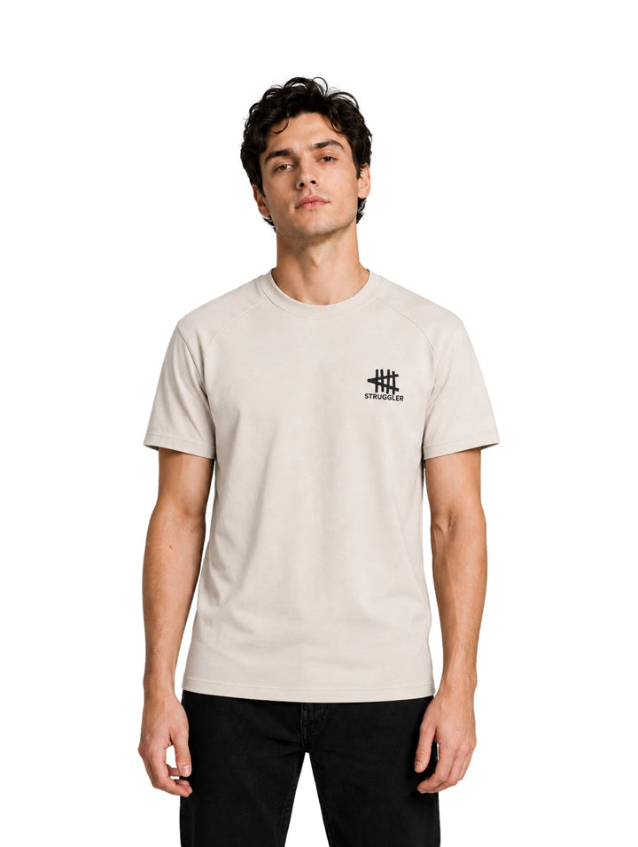 Hombre vistiendo playera de color hueso de manga corta con logotipo pequeño en el pecho.