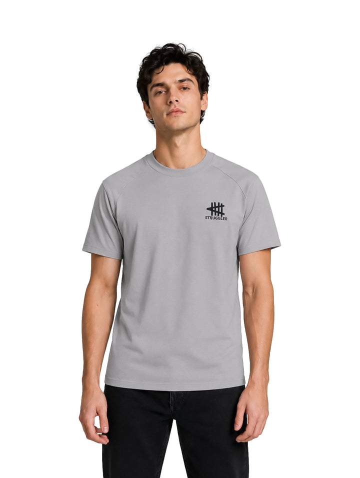 Hombre vistiendo una playera de color gris de manga corta con un pequeño logotipo negro en el pecho.