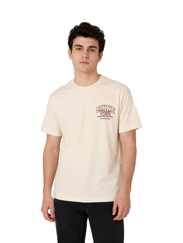Hombre vistiendo una playera color beige de manga corta con estampado en el pecho.