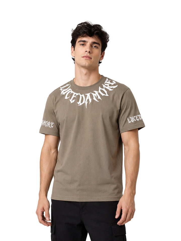 Hombre vistiendo playera color olive con letras blancas estilo gótico en el pecho y mangas.