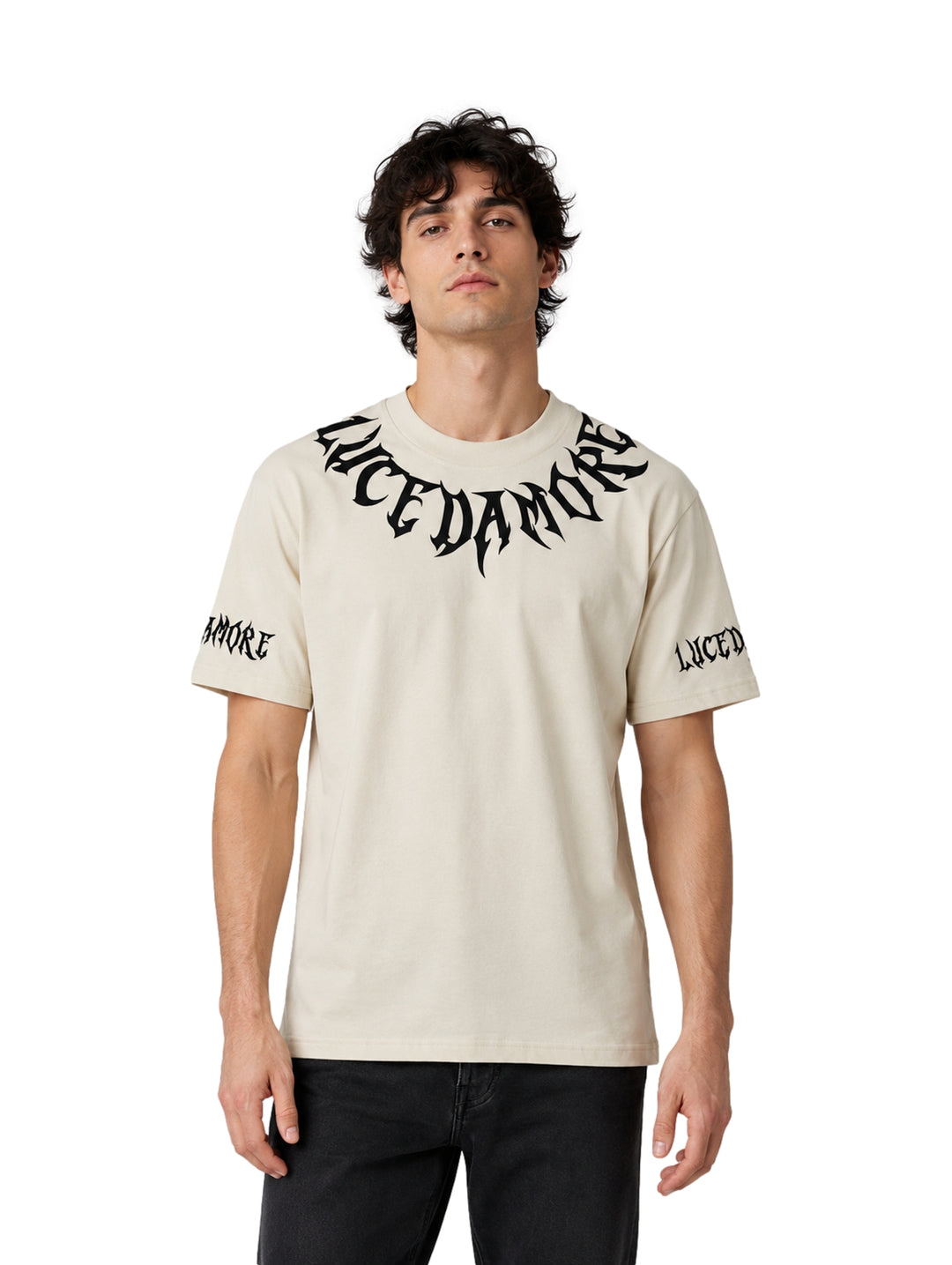 Hombre vistiendo playera color beige de manga corta con diseño de letras góticas negras en el cuello y mangas.