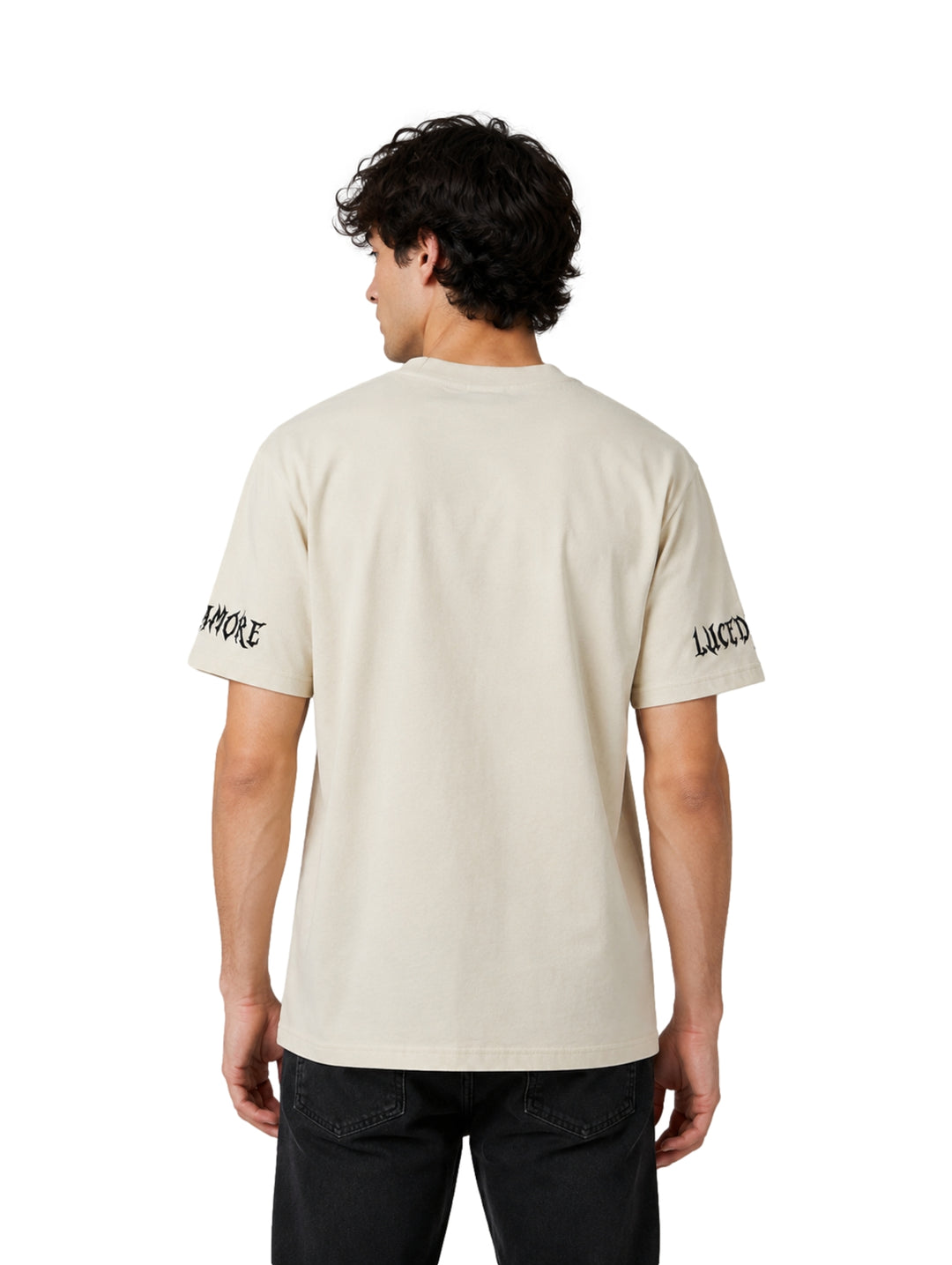 Hombre vistiendo playera color beige de manga corta con diseño de letras góticas negras en el cuello y mangas.