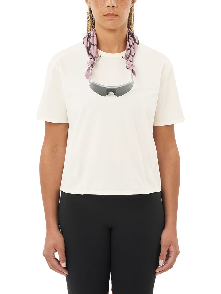 Mujer usando playera deportiva Salomon color beige y pantalones negros.