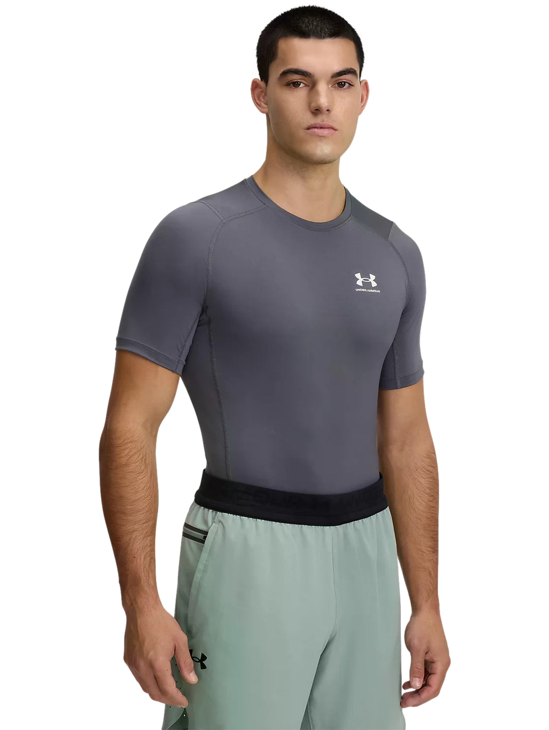 Hombre usando playera de compresión gris Under Armour y shorts deportivos verde claro.