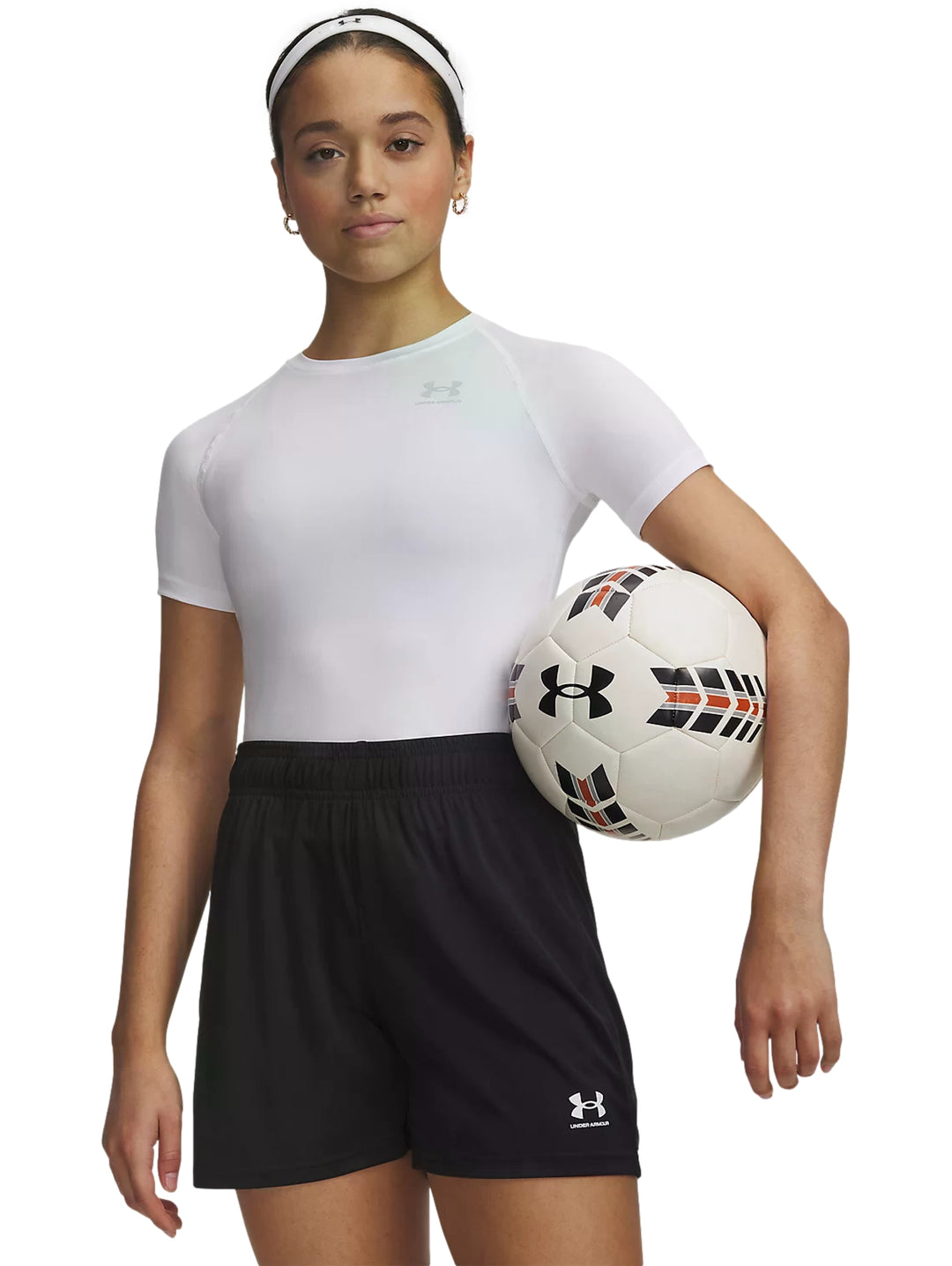 Mujer con playera blanca de compresión Under Armour, shorts negros y un balón de fútbol.