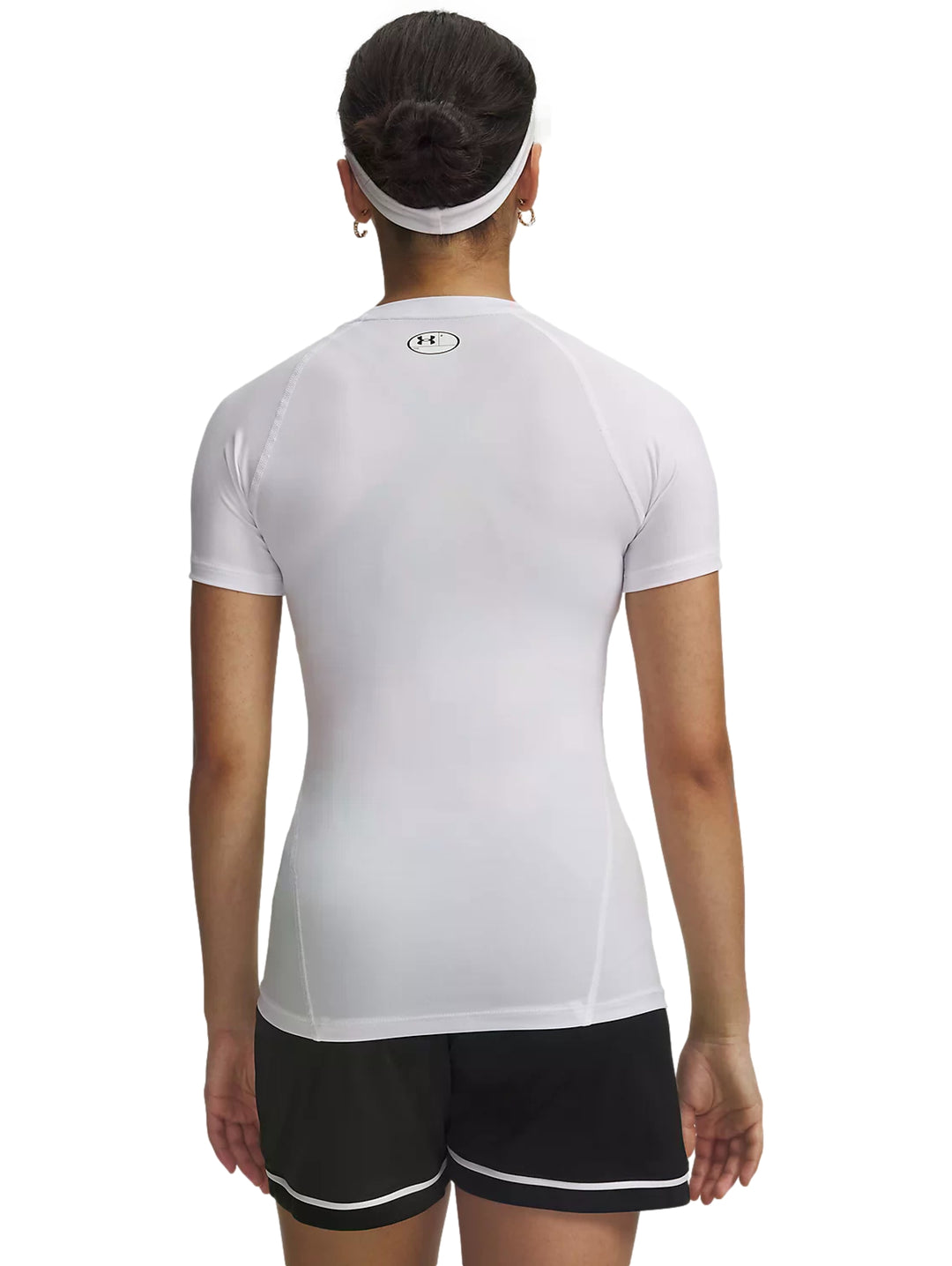 Mujer con playera blanca de compresión Under Armour, shorts negros y un balón de fútbol.