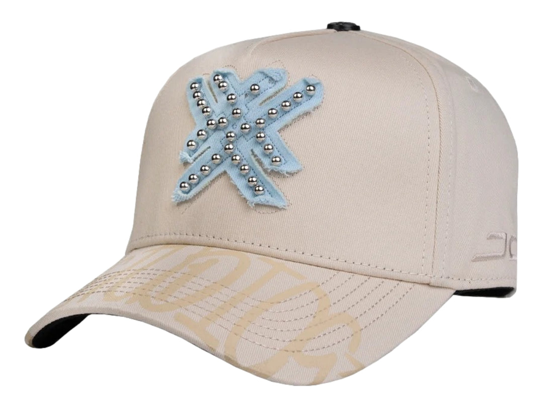 Gorra snapback color beige con un parche azul en forma de estrella decorado con perlas plateadas.