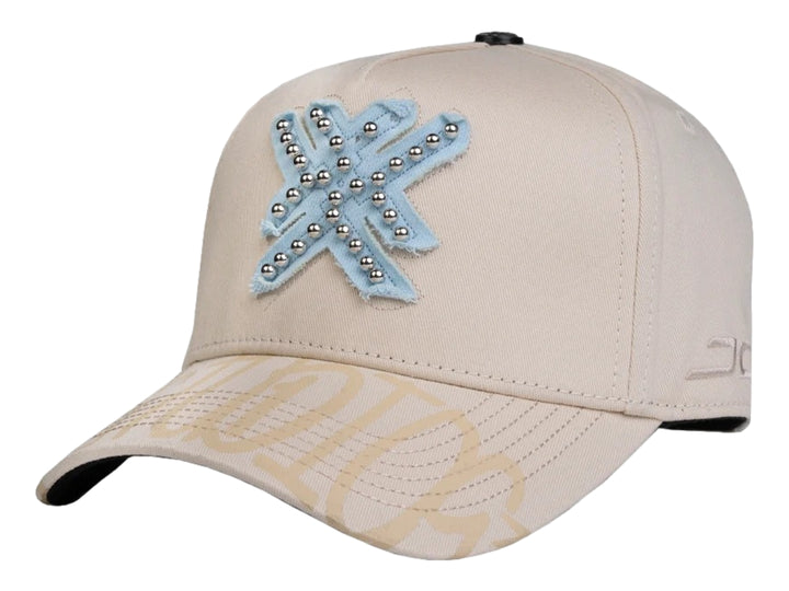 Gorra snapback color beige con un parche azul en forma de estrella decorado con perlas plateadas.