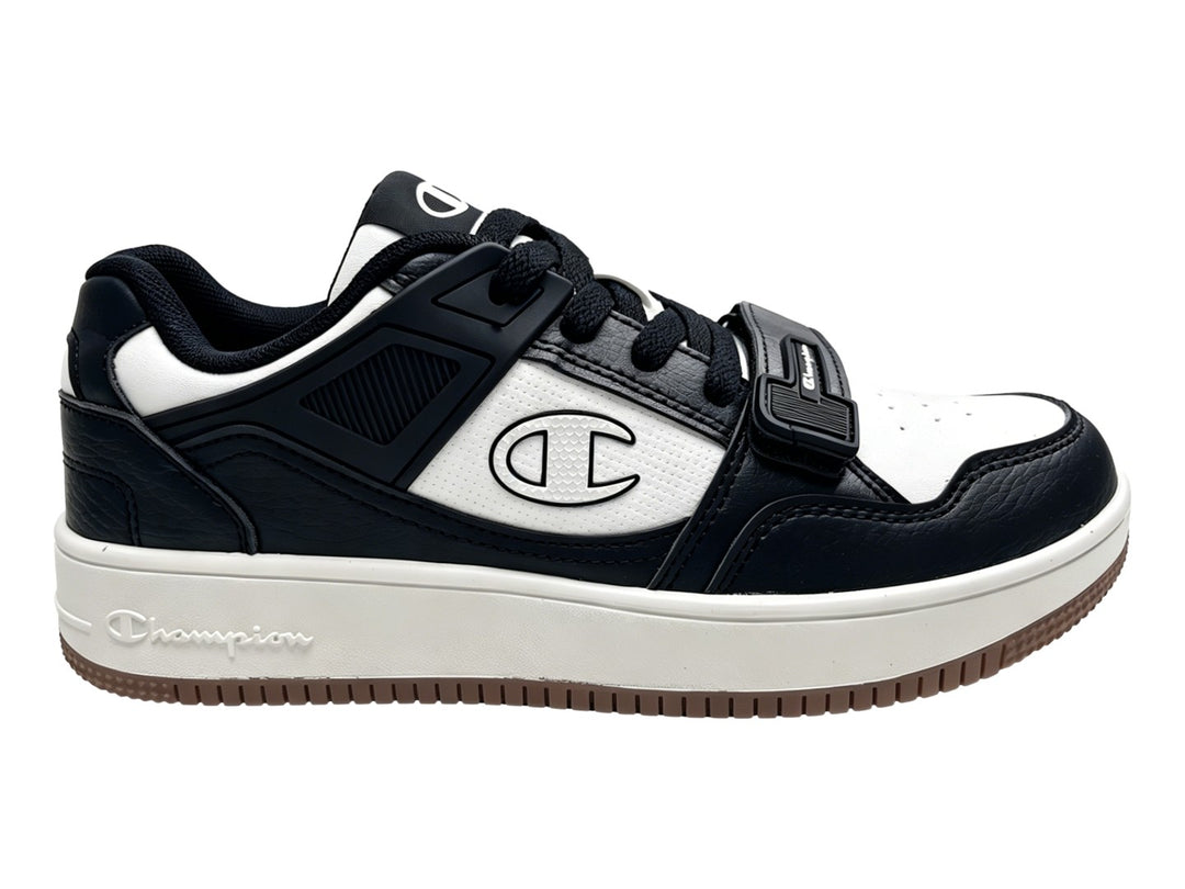 Tenis Champion Ace Cross en colores negro y blanco con suela blanca y detalle de correa velcro.