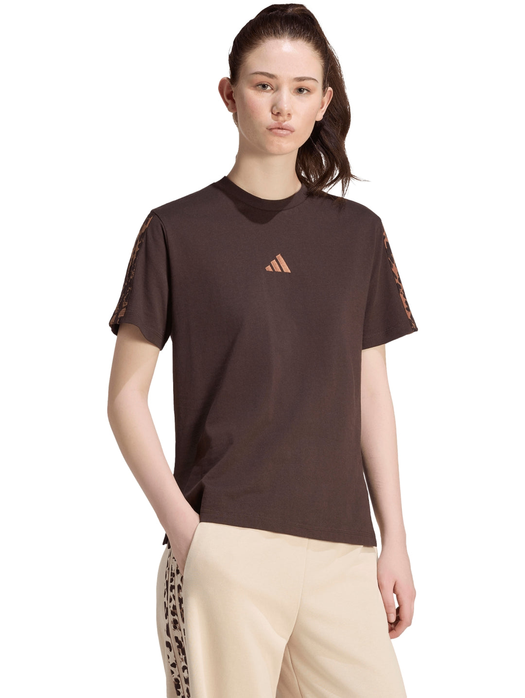 Mujer vistiendo playera Adidas color café oscuro con estampado en mangas y pantalones beige.
