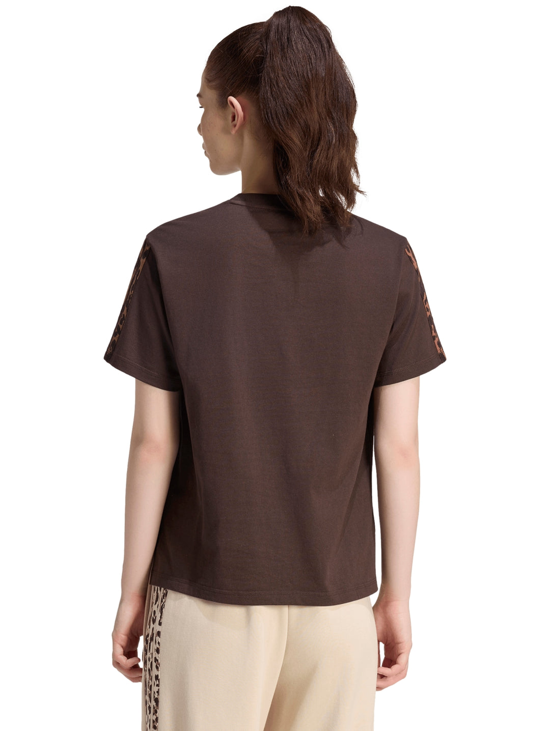 Mujer vistiendo playera Adidas color café oscuro con estampado en mangas y pantalones beige.