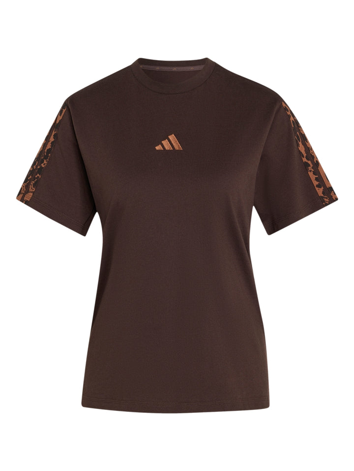 Mujer vistiendo playera Adidas color café oscuro con estampado en mangas y pantalones beige.