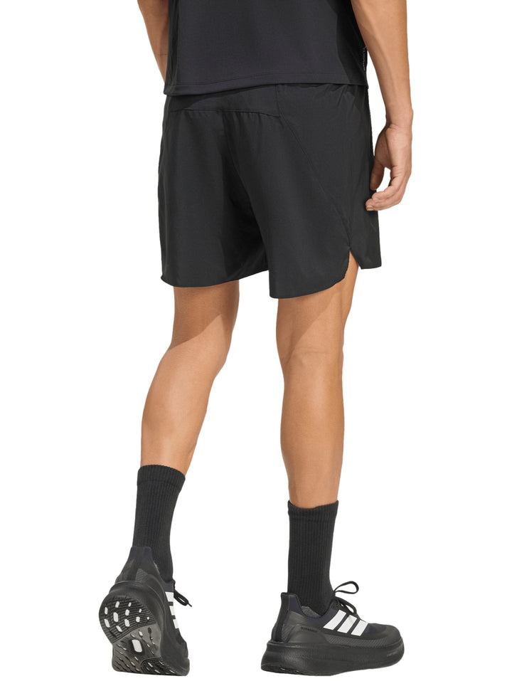 Hombre vistiendo shorts deportivos Adidas color negro, calcetines y tenis negros sobre fondo blanco.