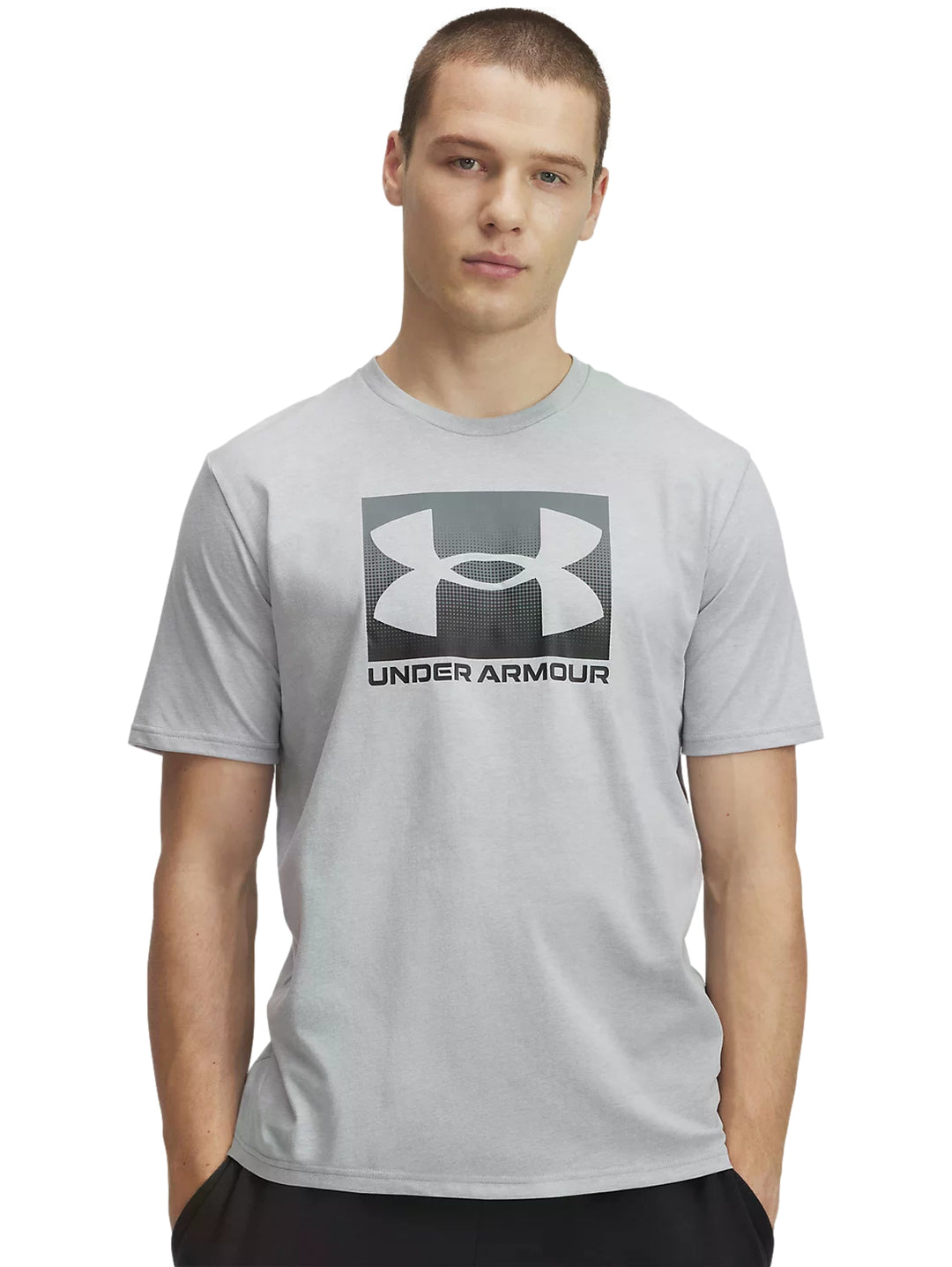 Hombre vistiendo playera deportiva Under Armour de color gris claro con logotipo negro en el pecho.