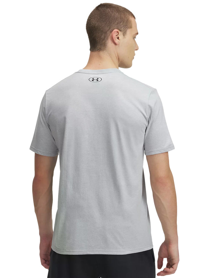 Hombre vistiendo playera deportiva Under Armour de color gris claro con logotipo negro en el pecho.