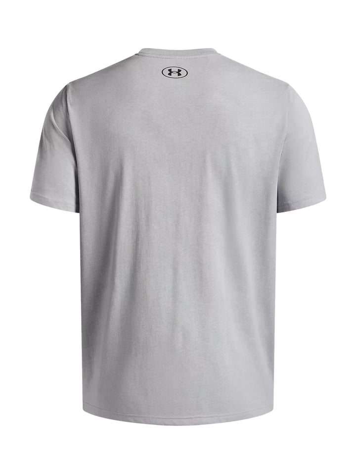 Hombre vistiendo playera deportiva Under Armour de color gris claro con logotipo negro en el pecho.