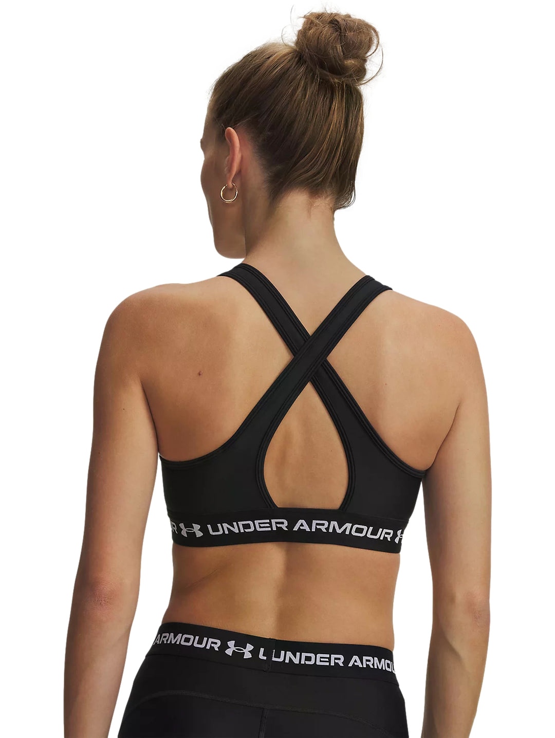 Mujer vistiendo un top deportivo negro de Under Armour con banda blanca en la base.