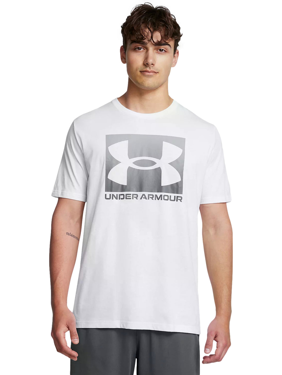 Hombre vistiendo playera deportiva blanca de manga corta con logotipo gris de Under Armour en el pecho.