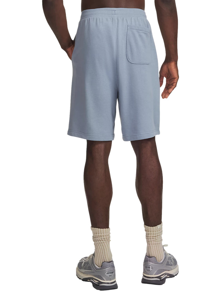 Hombre vistiendo shorts deportivos Under Armour color azul claro con calzado deportivo gris.