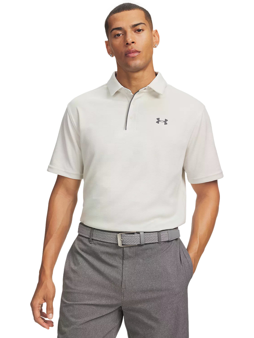 Hombre vistiendo playera polo blanca Under Armour y pantalones grises.