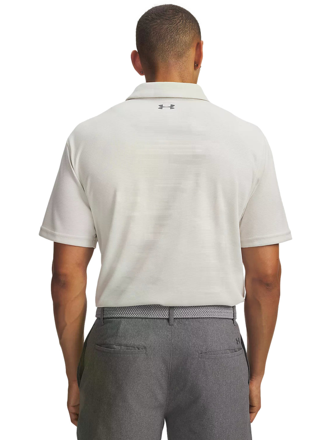Hombre vistiendo playera polo blanca Under Armour y pantalones grises.
