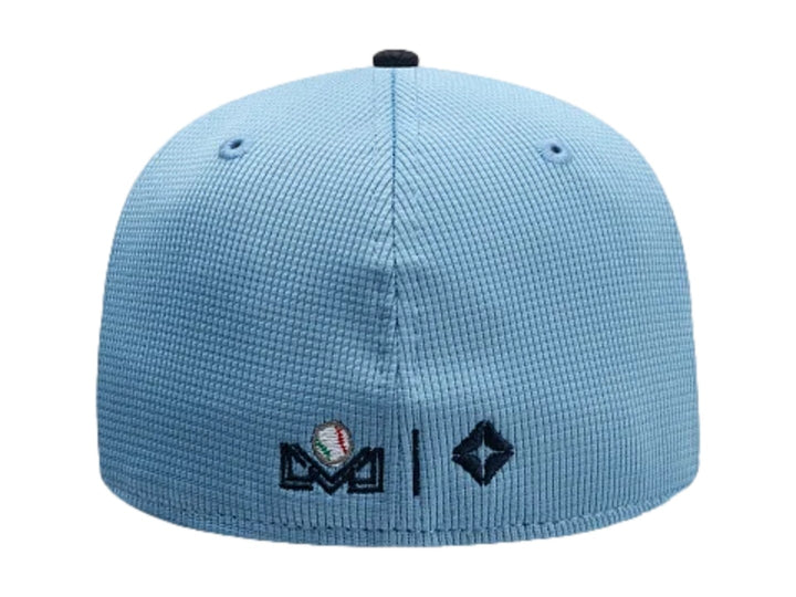 Gorra New Era 59Fifty con visera marino, paneles blanco y azul claro, y bordado frontal decorativo.