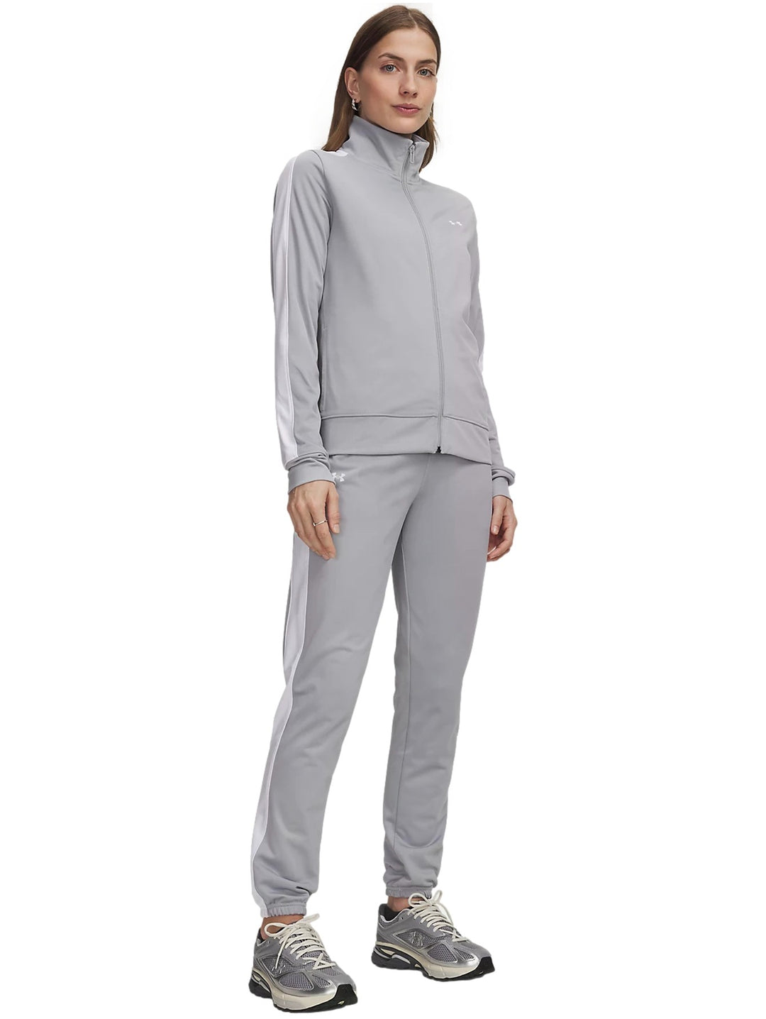 Mujer vistiendo conjunto deportivo Under Armour Tricot Tracksuit en color gris con detalles blancos.