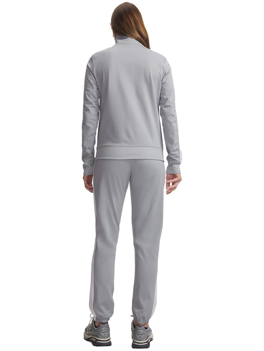 Mujer vistiendo conjunto deportivo Under Armour Tricot Tracksuit en color gris con detalles blancos.