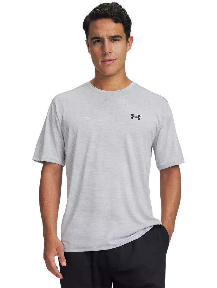 Hombre vistiendo playera deportiva Under Armour de color gris claro con logo negro en el pecho.