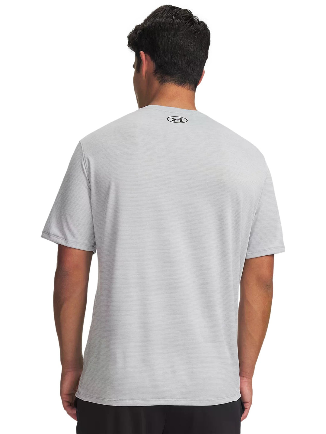 Hombre vistiendo playera deportiva Under Armour de color gris claro con logo negro en el pecho.