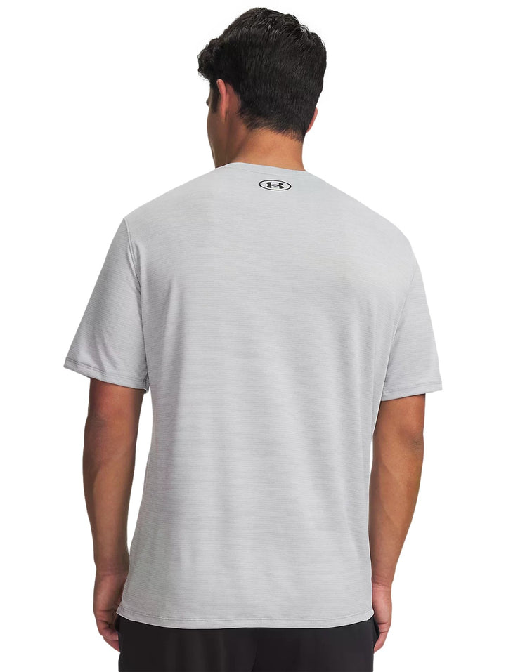 Hombre vistiendo playera deportiva Under Armour de color gris claro con logo negro en el pecho.