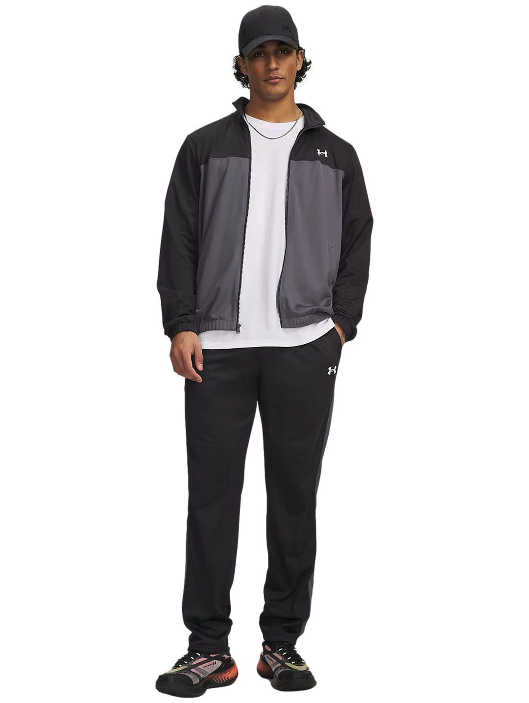 Hombre vistiendo conjunto deportivo Under Armour negro y gris con camiseta blanca y gorra negra.