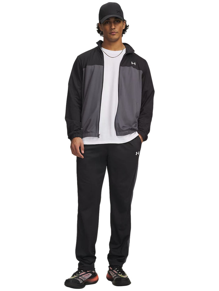 Hombre vistiendo conjunto deportivo Under Armour negro y gris con camiseta blanca y gorra negra.