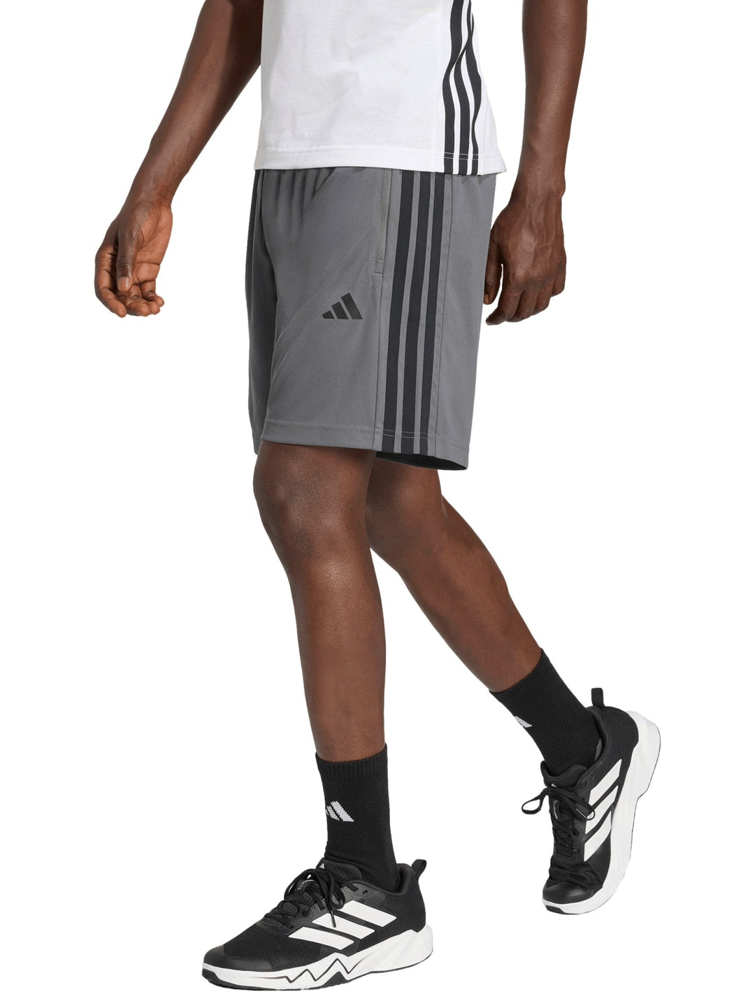 Hombre vistiendo short deportivo Adidas color gris con tres franjas negras laterales y logo frontal.