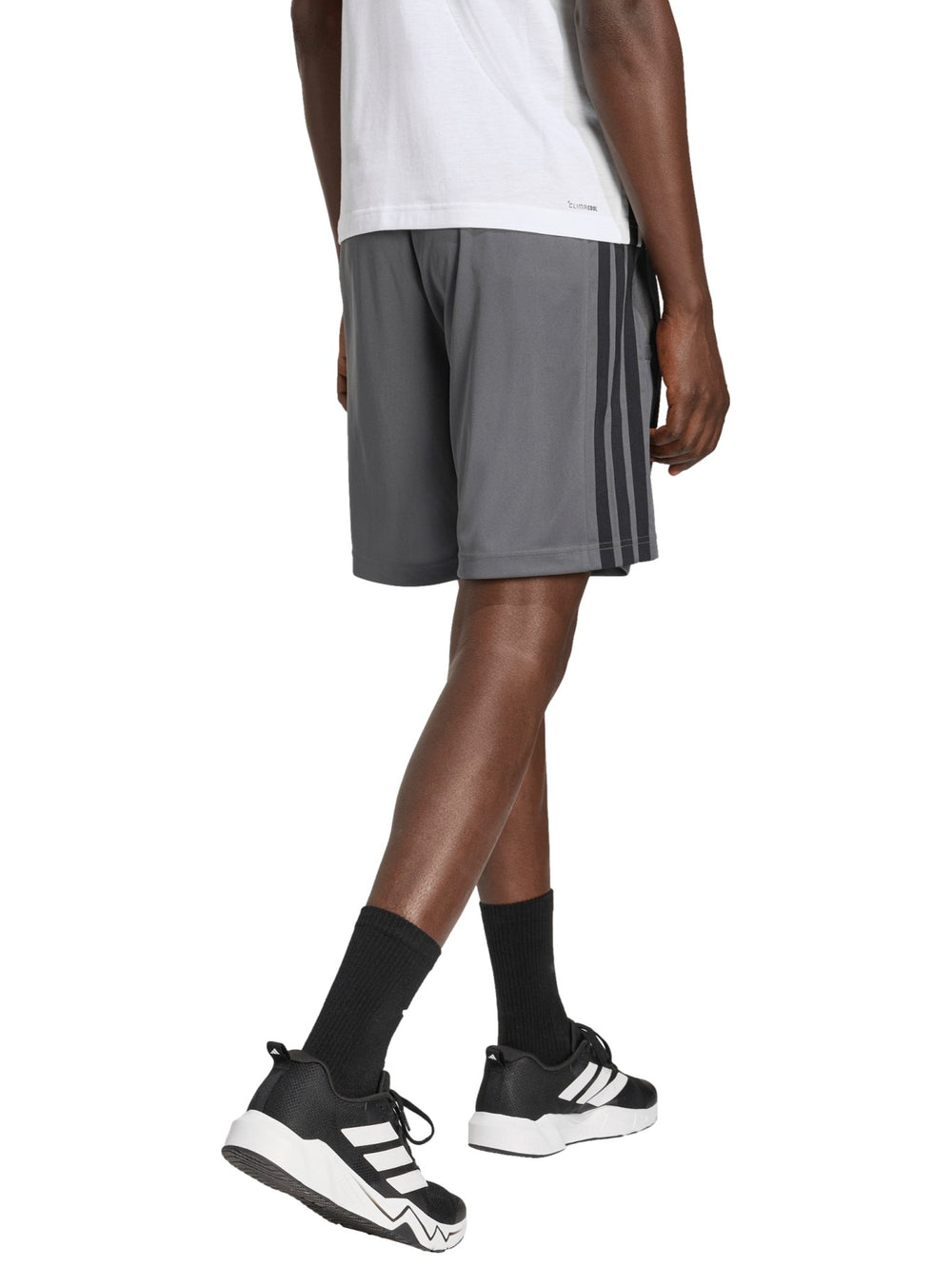 Hombre vistiendo short deportivo Adidas color gris con tres franjas negras laterales y logo frontal.