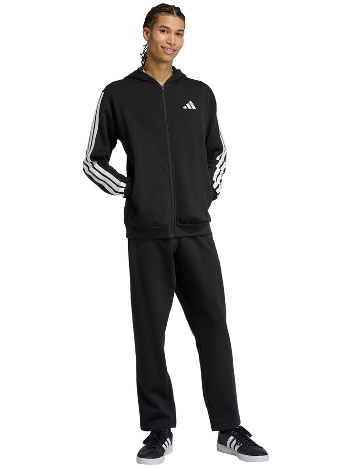 Hombre vistiendo conjunto deportivo Adidas negro con rayas blancas laterales, compuesto por sudadera con capucha y pantalón.