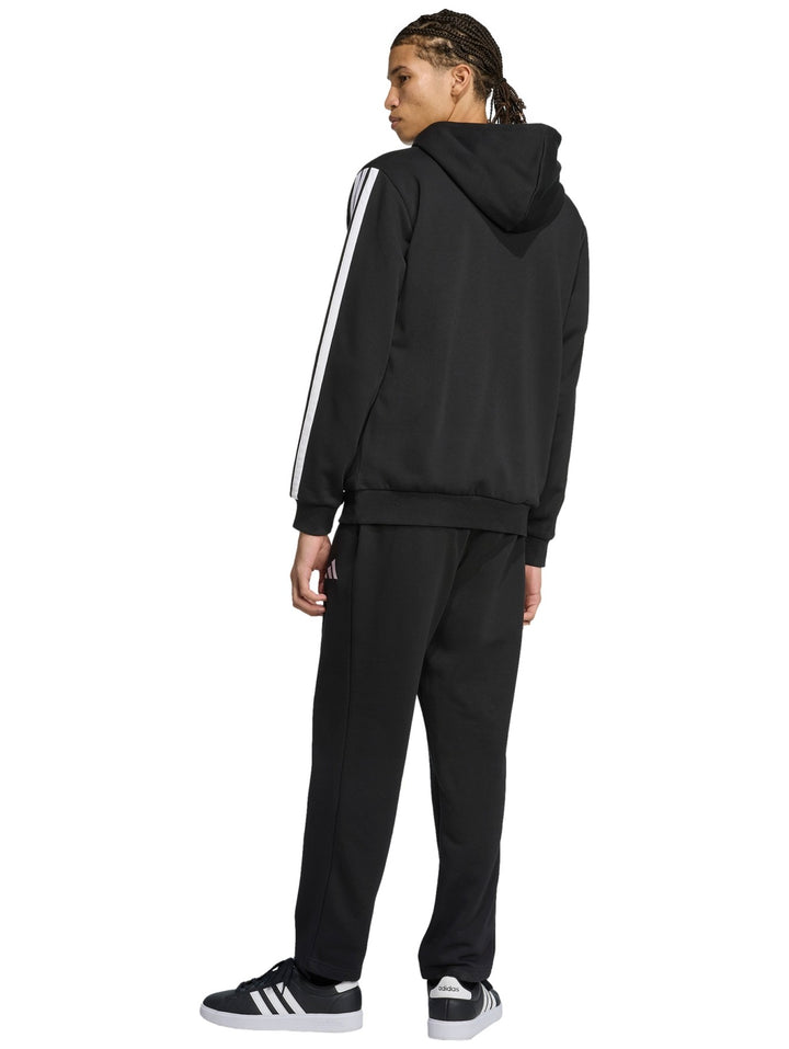 Hombre vistiendo conjunto deportivo Adidas negro con rayas blancas laterales, compuesto por sudadera con capucha y pantalón.