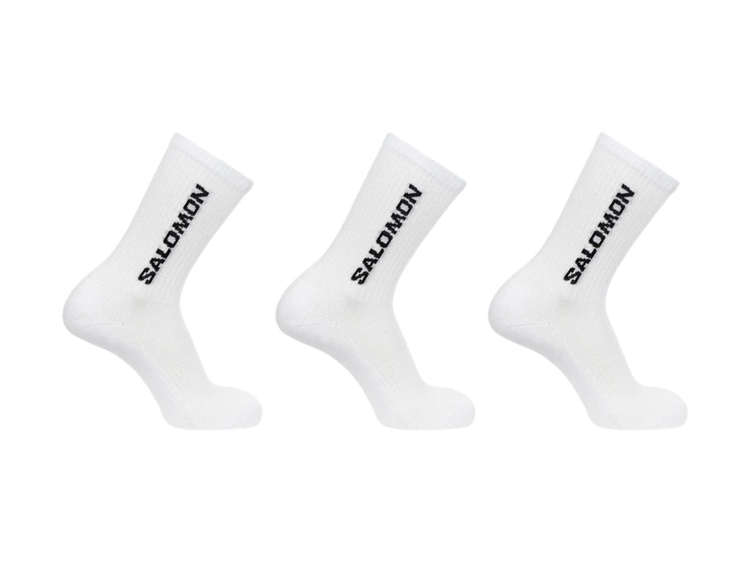 Paquete de tres calcetines blancos de caña media marca Salomon con logotipo negro vertical.
